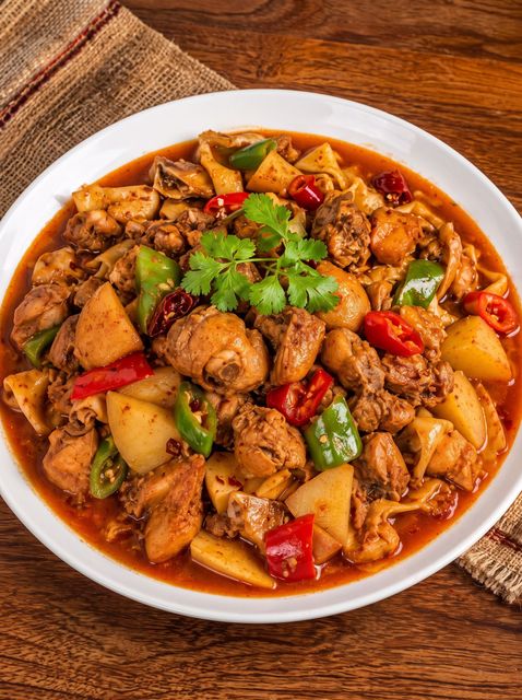 Red chicken and potato stew garnished with cilantro in a white bowl on a wooden table