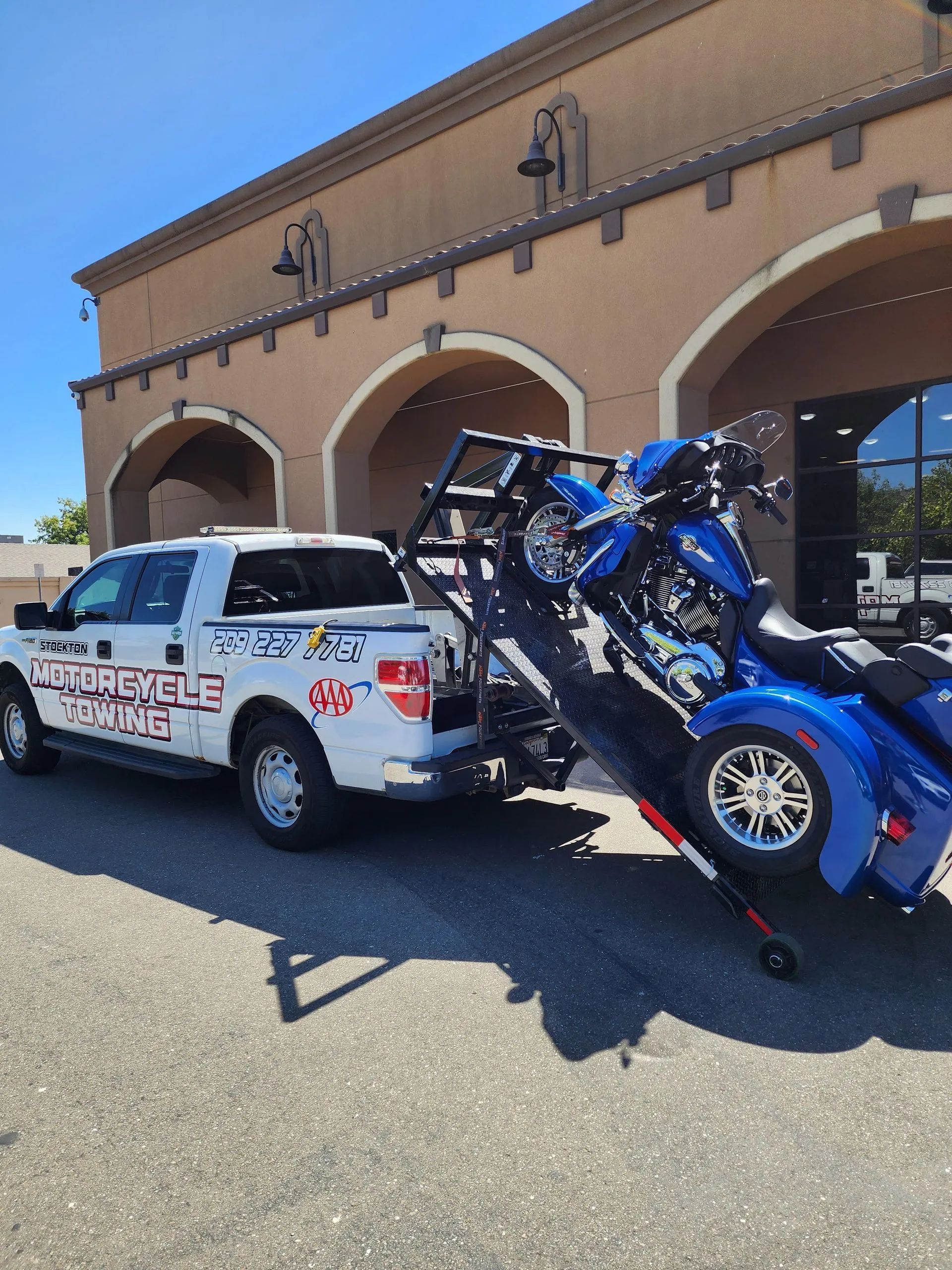 White pickup truck towing a blue motorcycle on a trailer in front of a building.