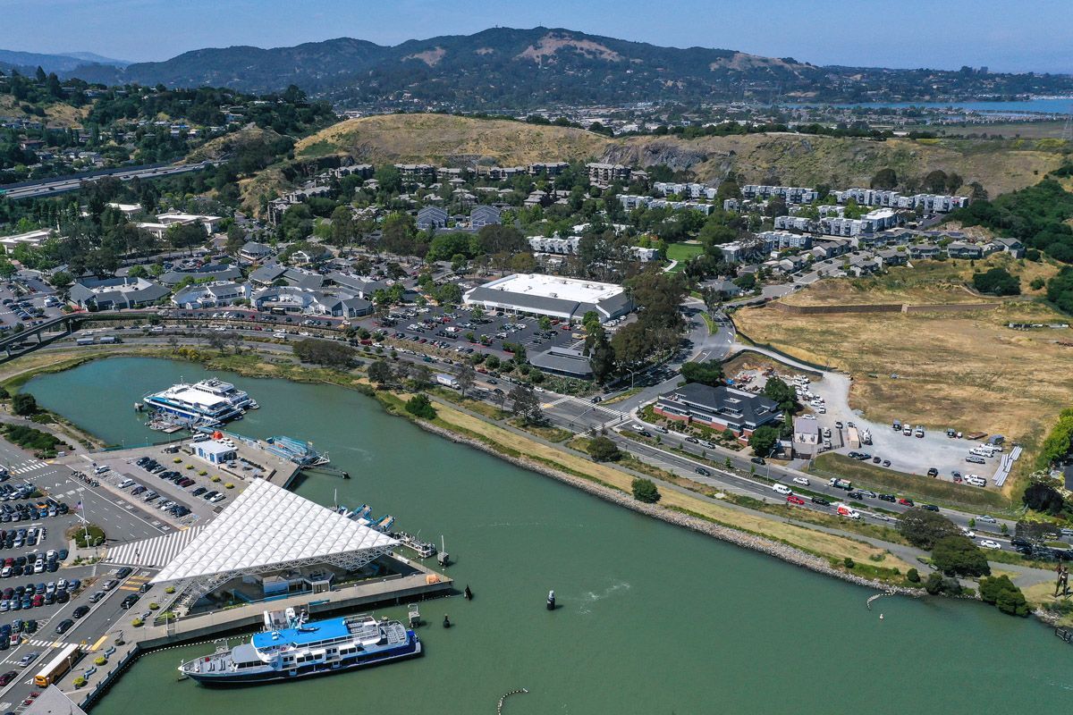Aerial view of a waterfront apartment community with marina, parking, and surrounding hills. Visit us at Finch at Larkspur and view pet-friendly 1 and 2 bedroom apartments and townhomes in Larkspur, CA.