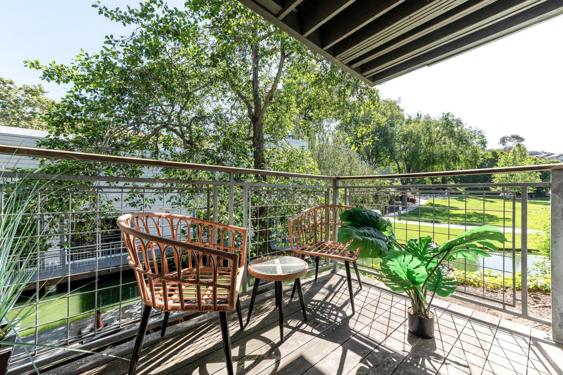 Balcony with wooden chair, table, and potted plant overlooking a sunny green garden