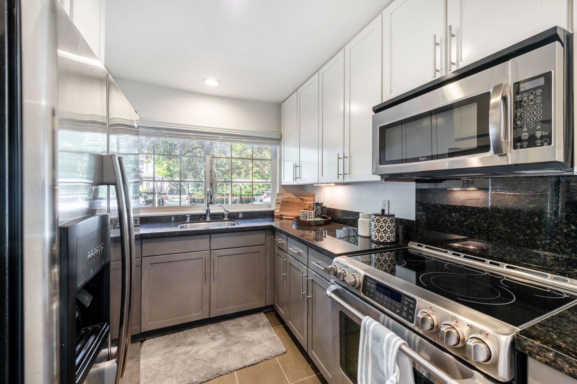Modern kitchen with stainless steel appliances, white cabinets, black countertops, and a window over the sink.