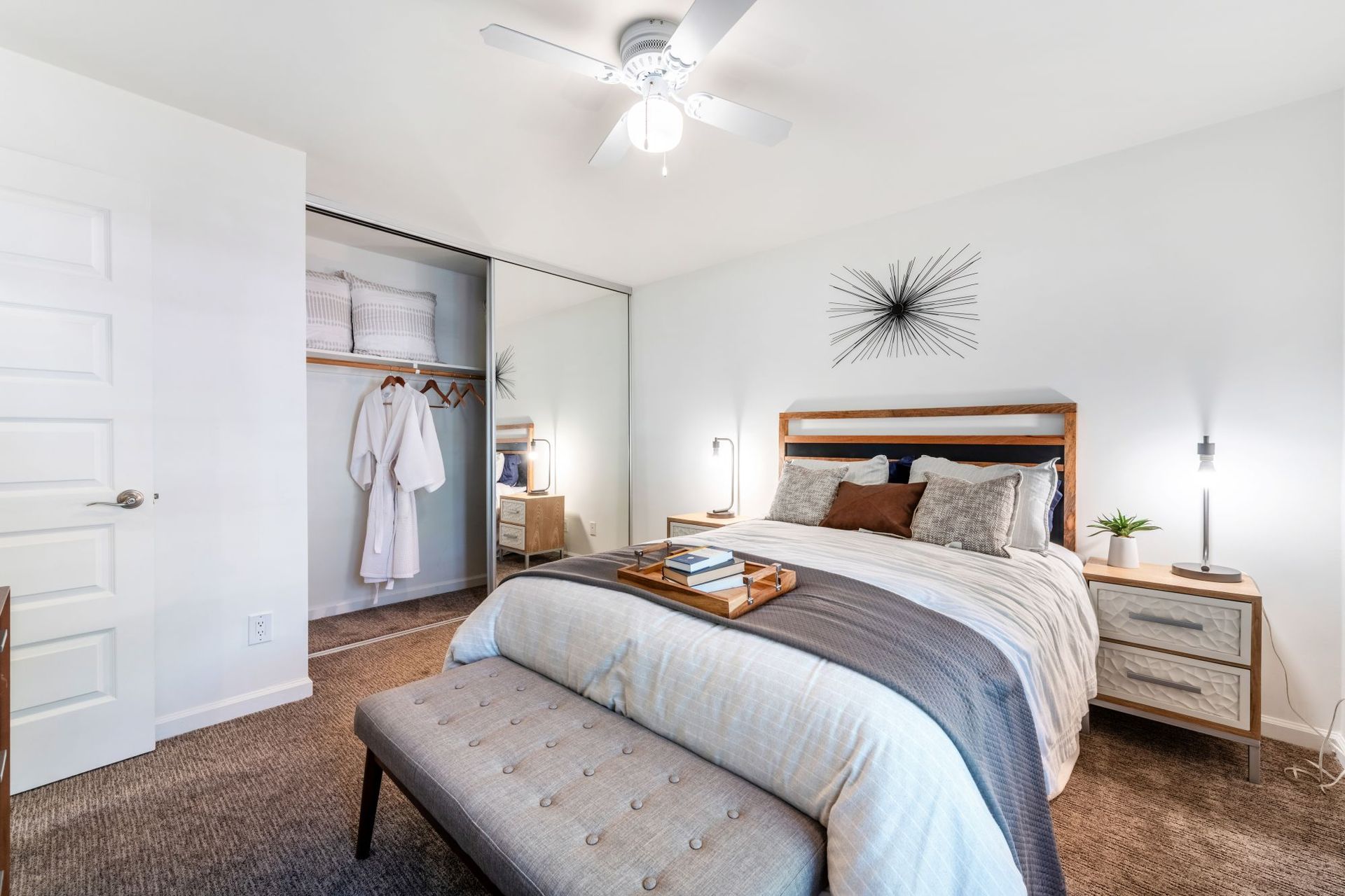 Bright bedroom with a bed, bench, closet, white walls, and ceiling fan