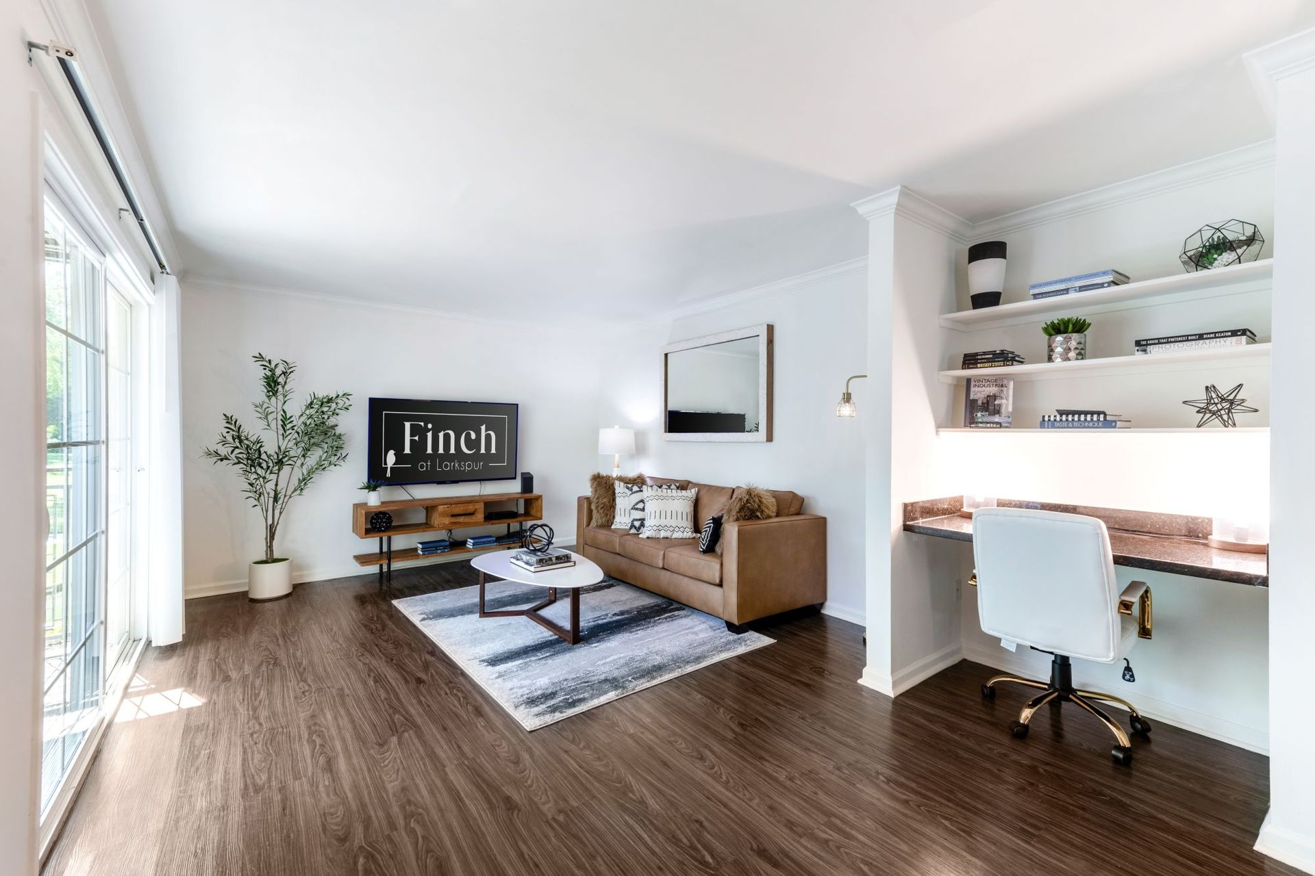 Bright living room with brown sofa, coffee table, rug, desk nook, and large sliding glass door
