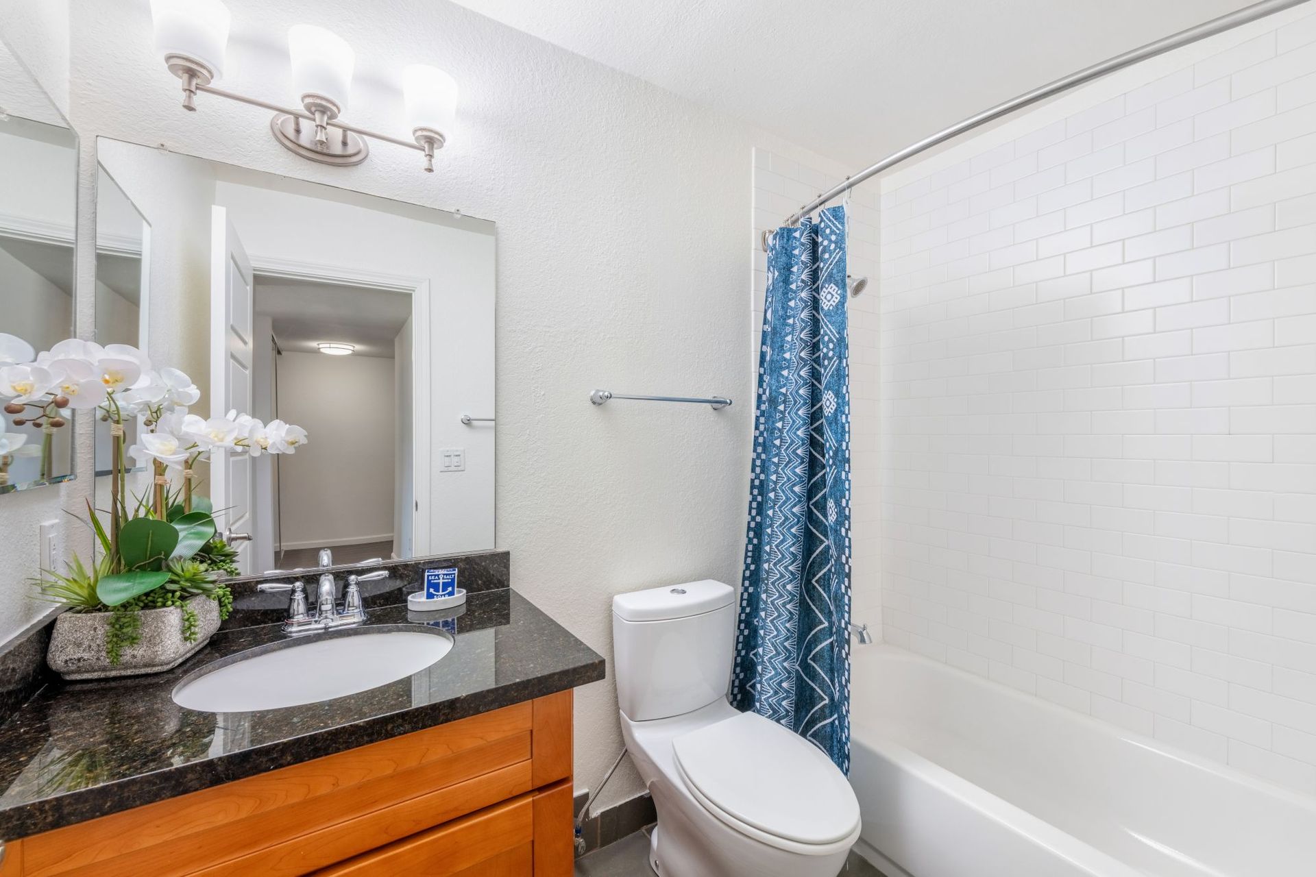 Modern white bathroom with granite vanity, mirror, toilet, tub, and blue shower curtain