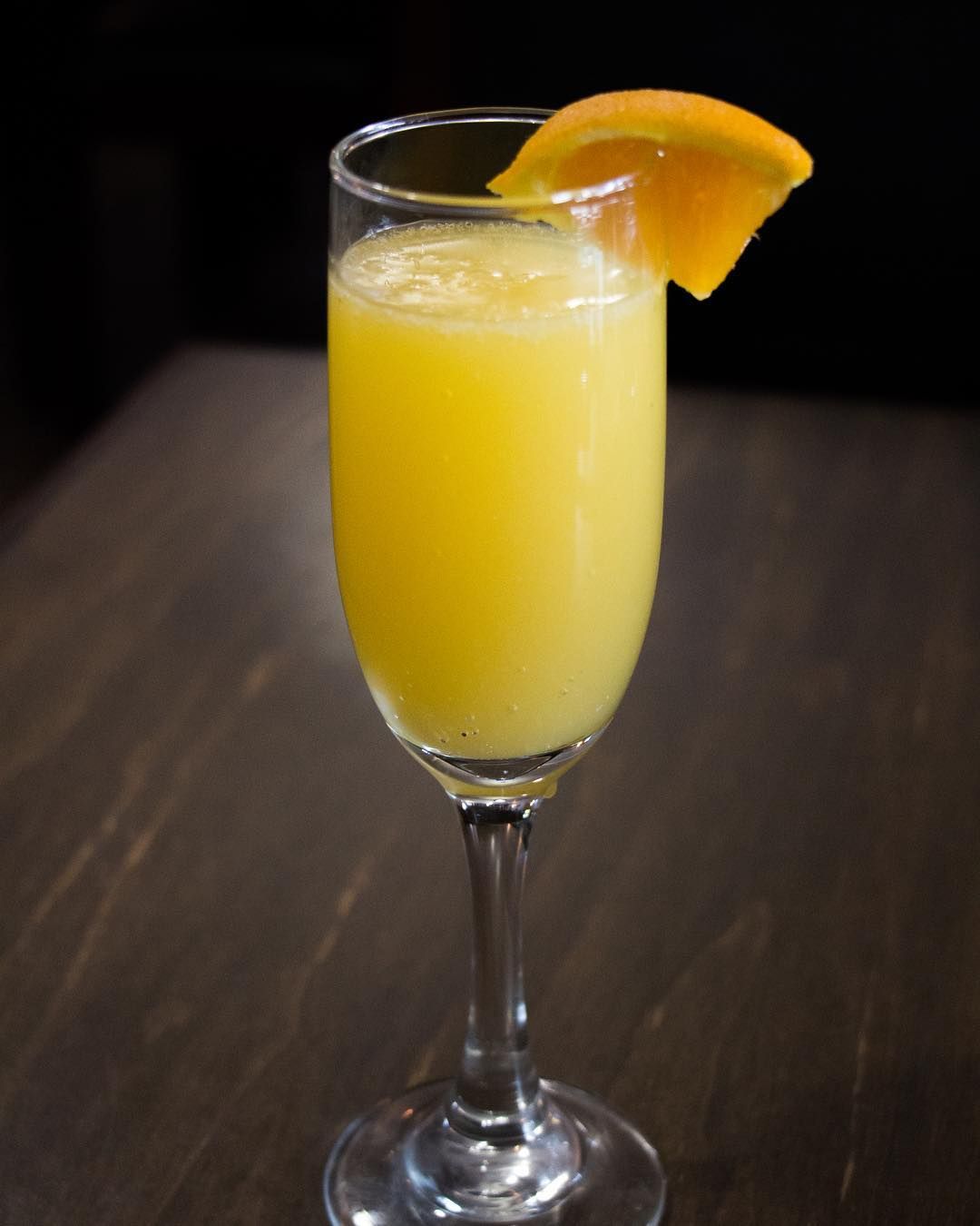 Coffee cocktail in tall glass, topped with foam, orange peel garnish, coffee beans, on gray surface.