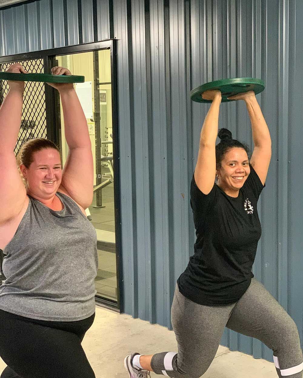 Two Women Are Lifting Weights Over Their Heads In Front Of A Building — Elev8ed Fitness In Currajong, QLD