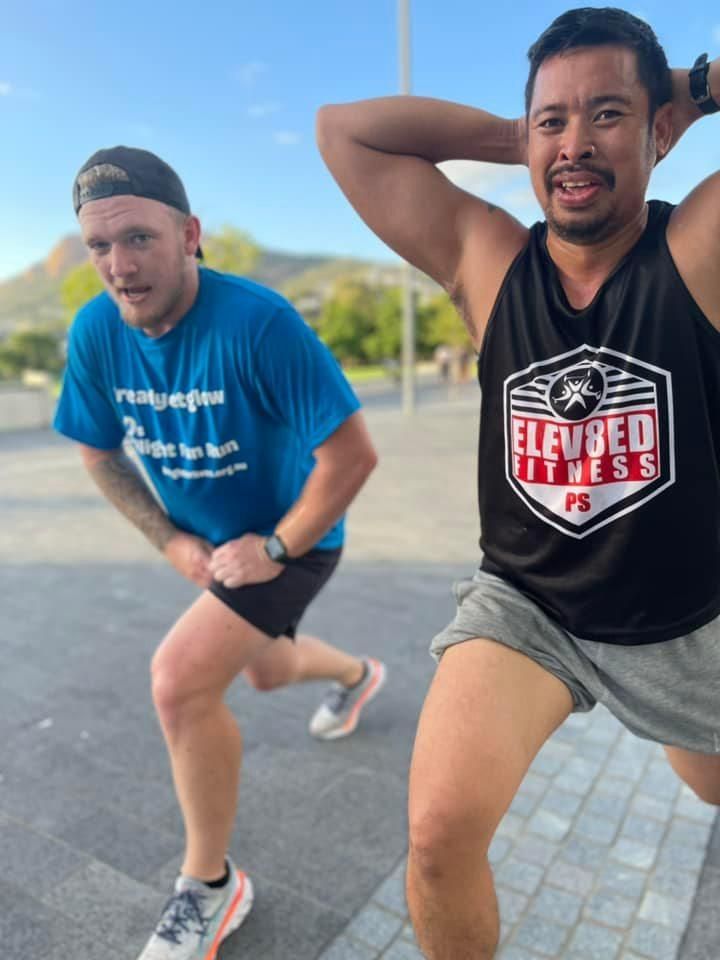 A Man Wearing A Black Elevated Fitness Tank Top Is Squatting Next To Another Man — Elev8ed Fitness In Currajong, QLD