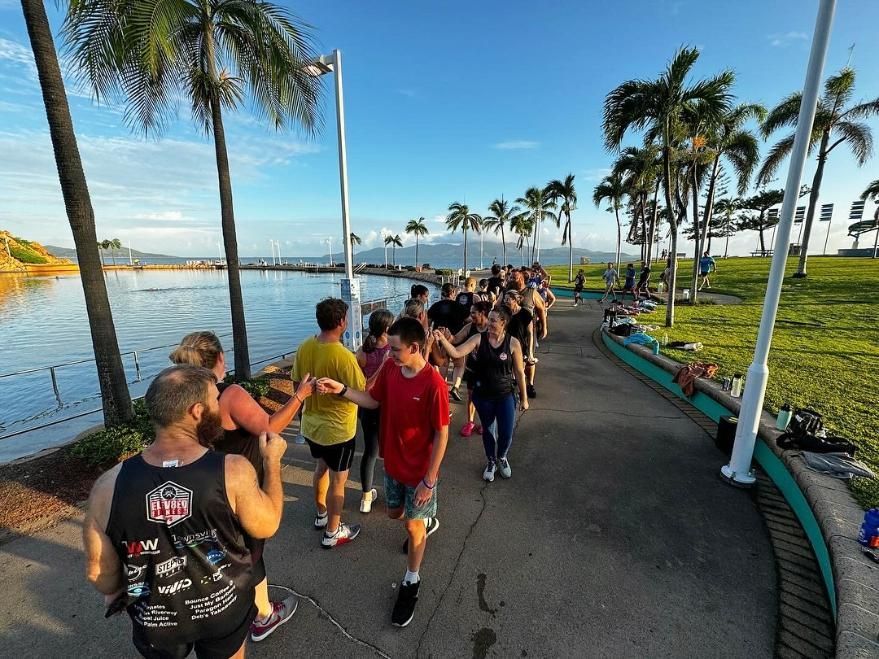 A Group Of People Are Walking Down A Sidewalk Next To A Body Of Water — Elev8ed Fitness In Currajong, QLD