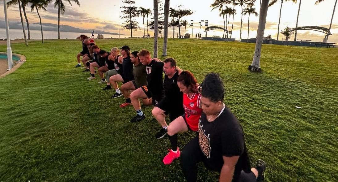 A Group Of People Are Squatting On The Grass In A Park — Elev8ed Fitness In Currajong, QLD