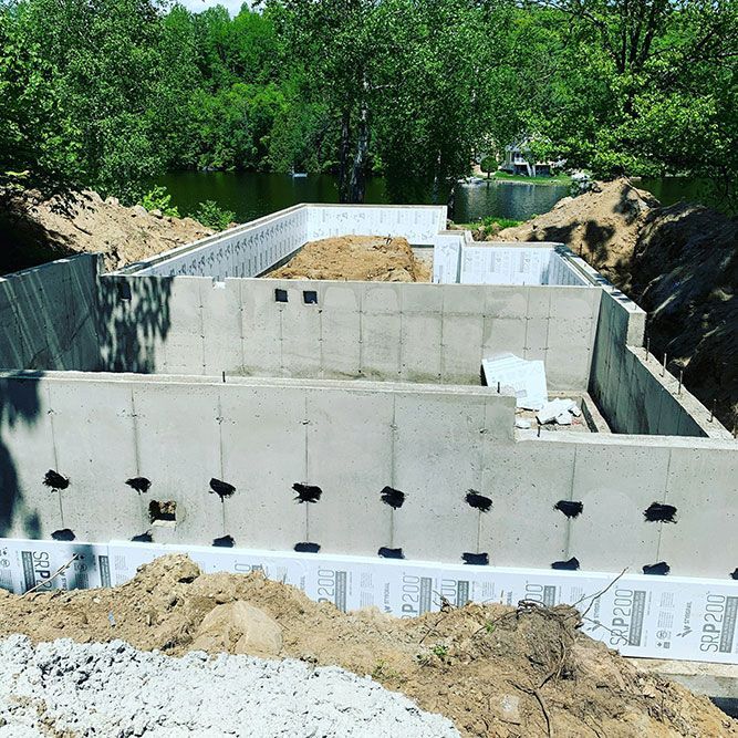 Des murs de fondation en béton sont construits sur un terrain excavé, entourés de terre et d'isolant.