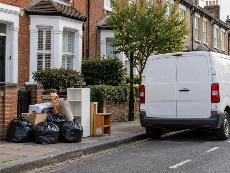 Bulky items and bags left by a front wall with a van parked alongside