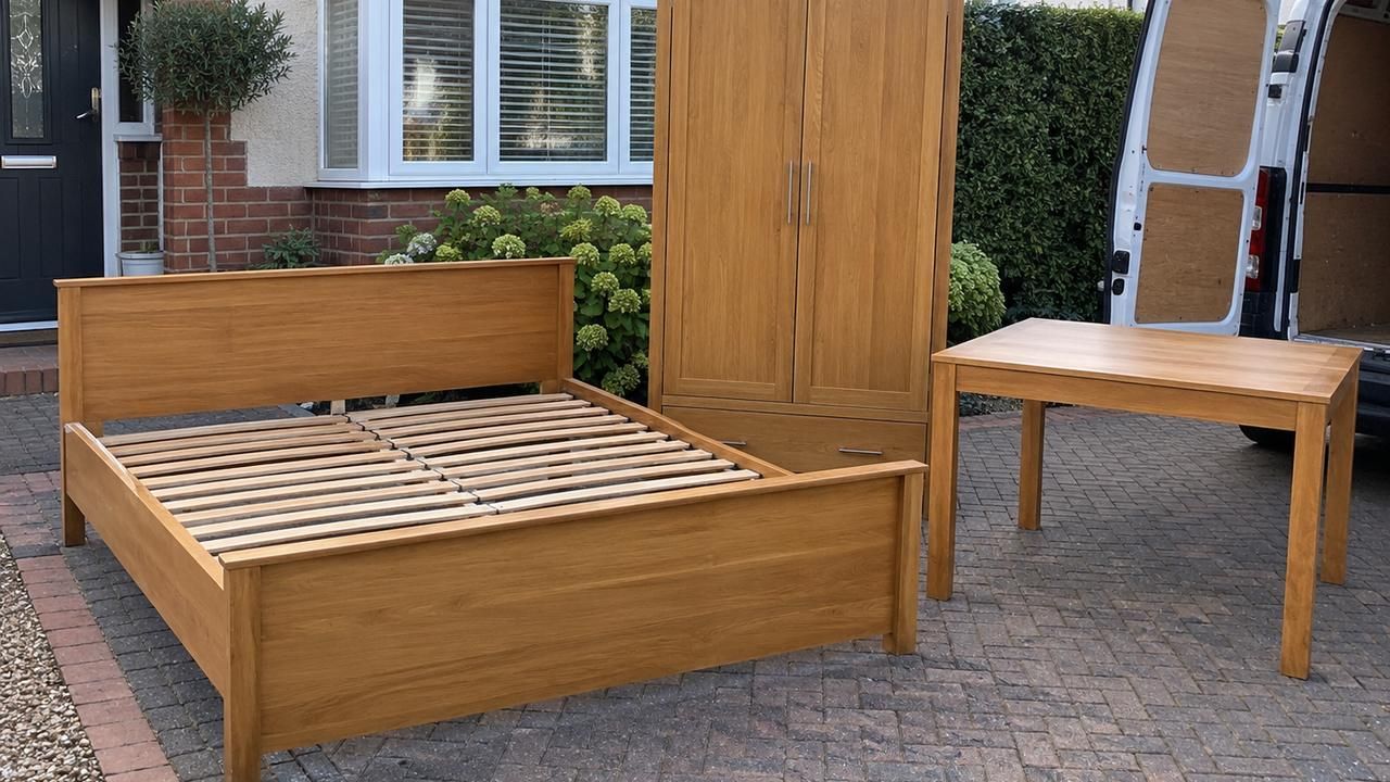 Bed frame, wardrobe and table on a driveway beside a van