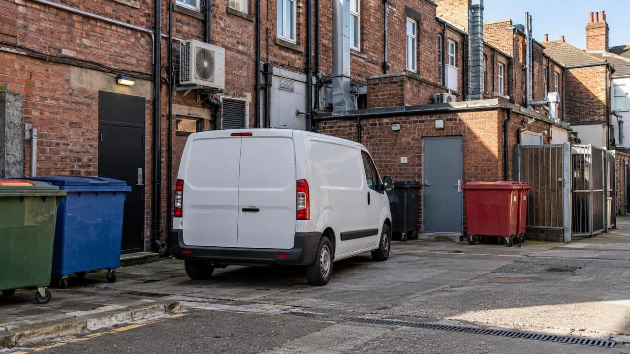 Van parked in a service yard beside commercial wheelie bins