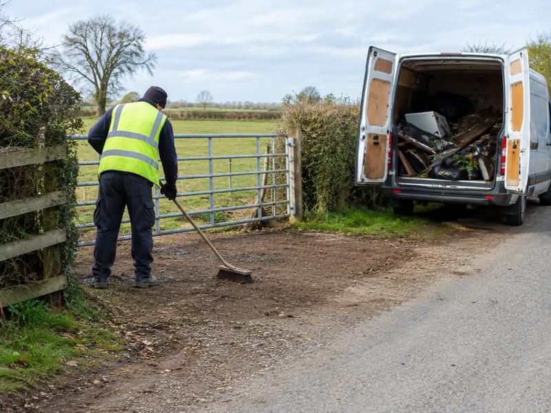 Worker sweeping a gateway clean after fly-tipped waste has been loaded