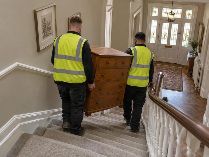 Two workers carrying a chest of drawers down a staircase
