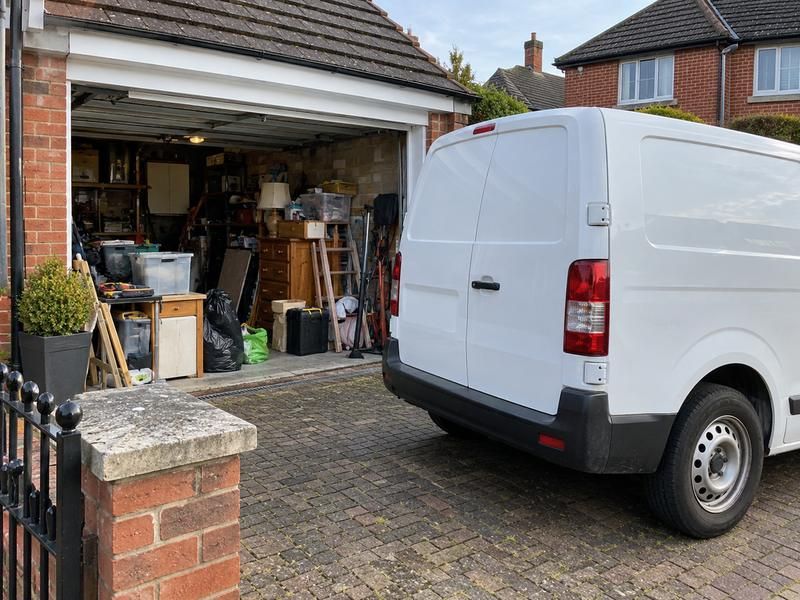 Garage full of boxes, tools and old furniture with a van parked outside