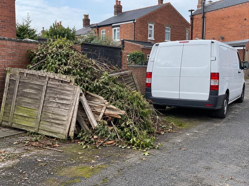 Pile of hedge cuttings and old fence panels beside a van