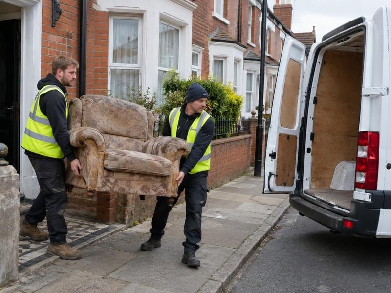Two workers carrying an armchair out of a terraced house to the van