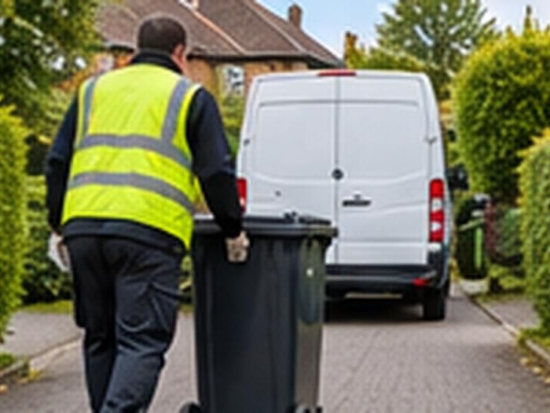 Worker wheeling a full wheelie bin down a path to a van