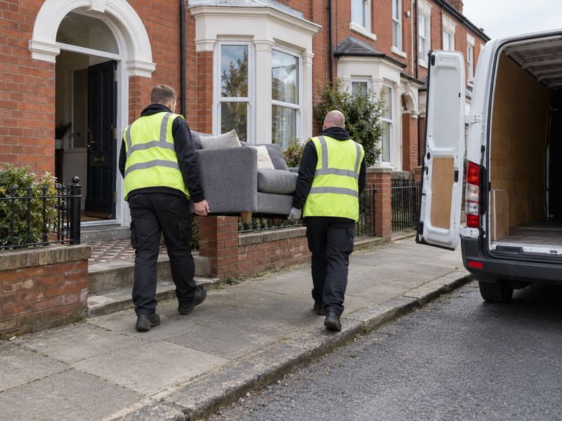 Two workers carrying an old sofa out to a van