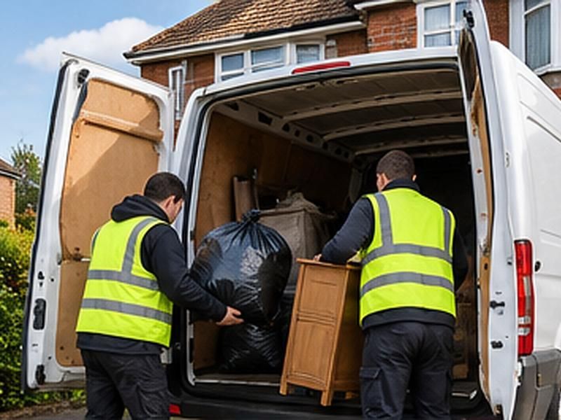 Two workers loading bags and furniture into a van outside a house