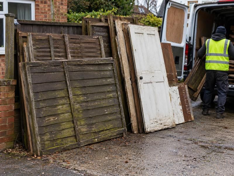 Old doors and fence panels stacked against a fence