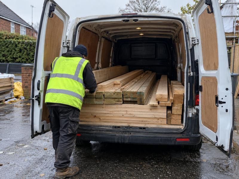 Worker loading lengths of timber into a van