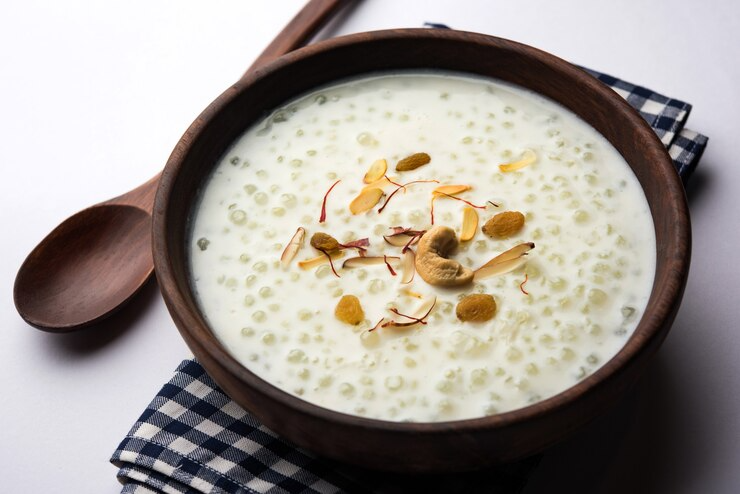 Bowl of creamy rice pudding topped with almonds on a checkered cloth, with a wooden spoon nearby