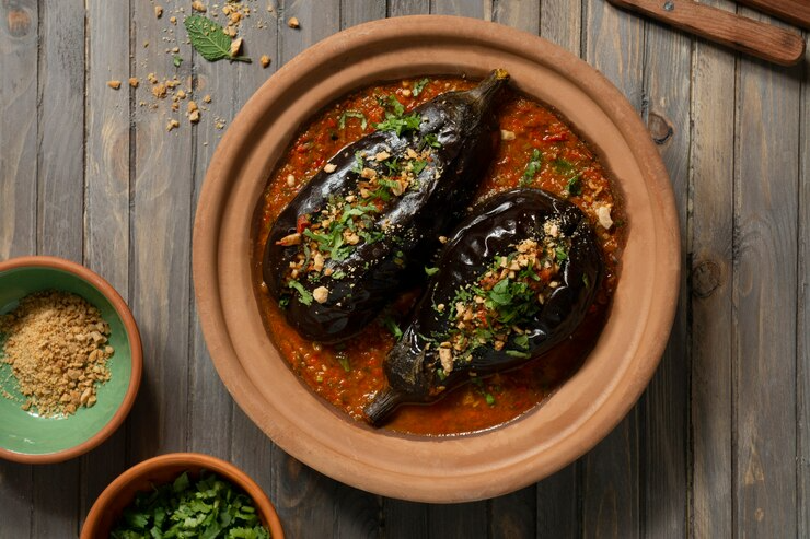 Two roasted eggplants in sauce on a terracotta plate, topped with herbs on a rustic wooden table