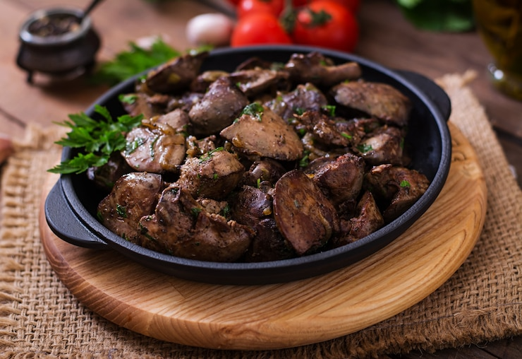 Grilled meat chunks in a black skillet on a wooden board, garnished with parsley