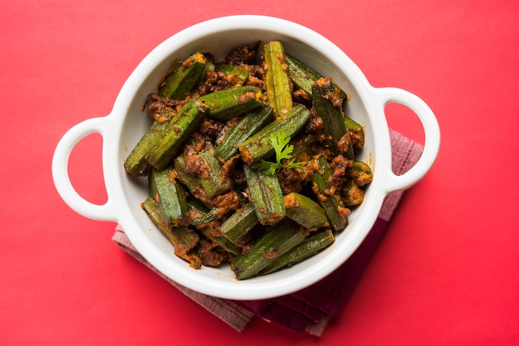 White bowl of spiced okra on a red background