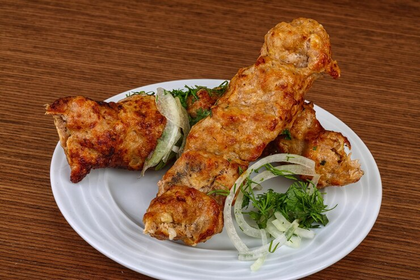 Plate of grilled tandoori chicken with sliced onions and herbs on a wooden table