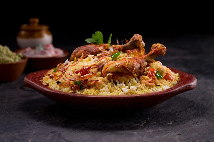 Plate of rice topped with roasted chicken and herbs on a dark table, with a blurred side dish in the background