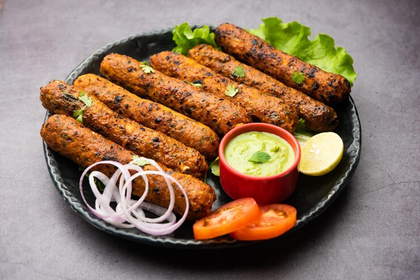Grilled kebabs on a black plate with onions, tomato slices, lettuce, and chutney on the side