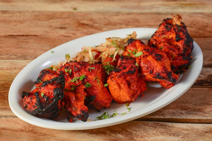 Plate of grilled red chicken tikka with herbs on a white dish, served on a wooden table