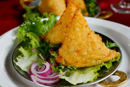 Two triangular samosas on a plate with lettuce and red onion slices