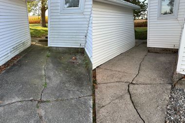 Cracked concrete walkway between white-sided buildings, with uneven pavement and a slanted wall panel.
