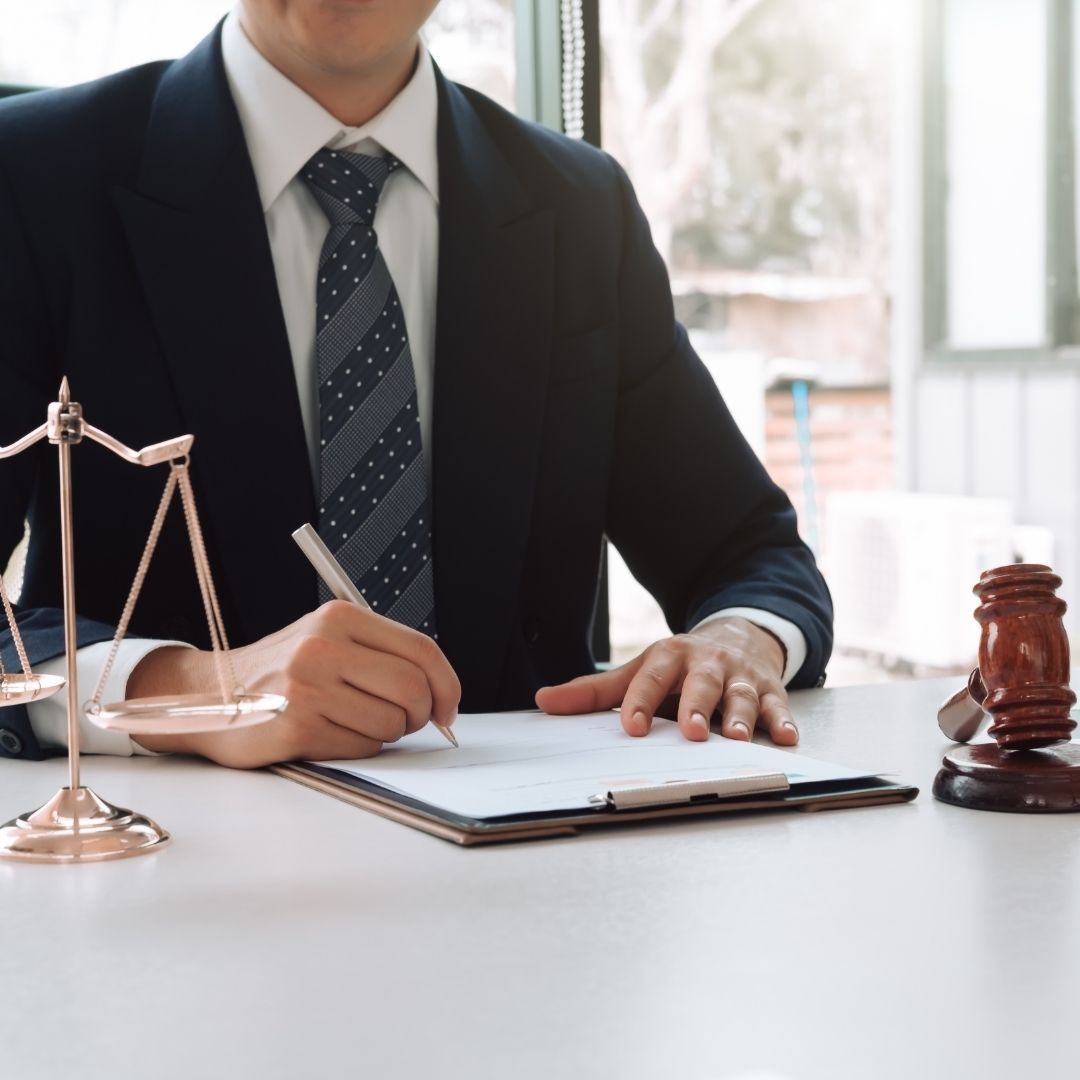 Lawyer in suit writing on a document at a desk with scales of justice and gavel.