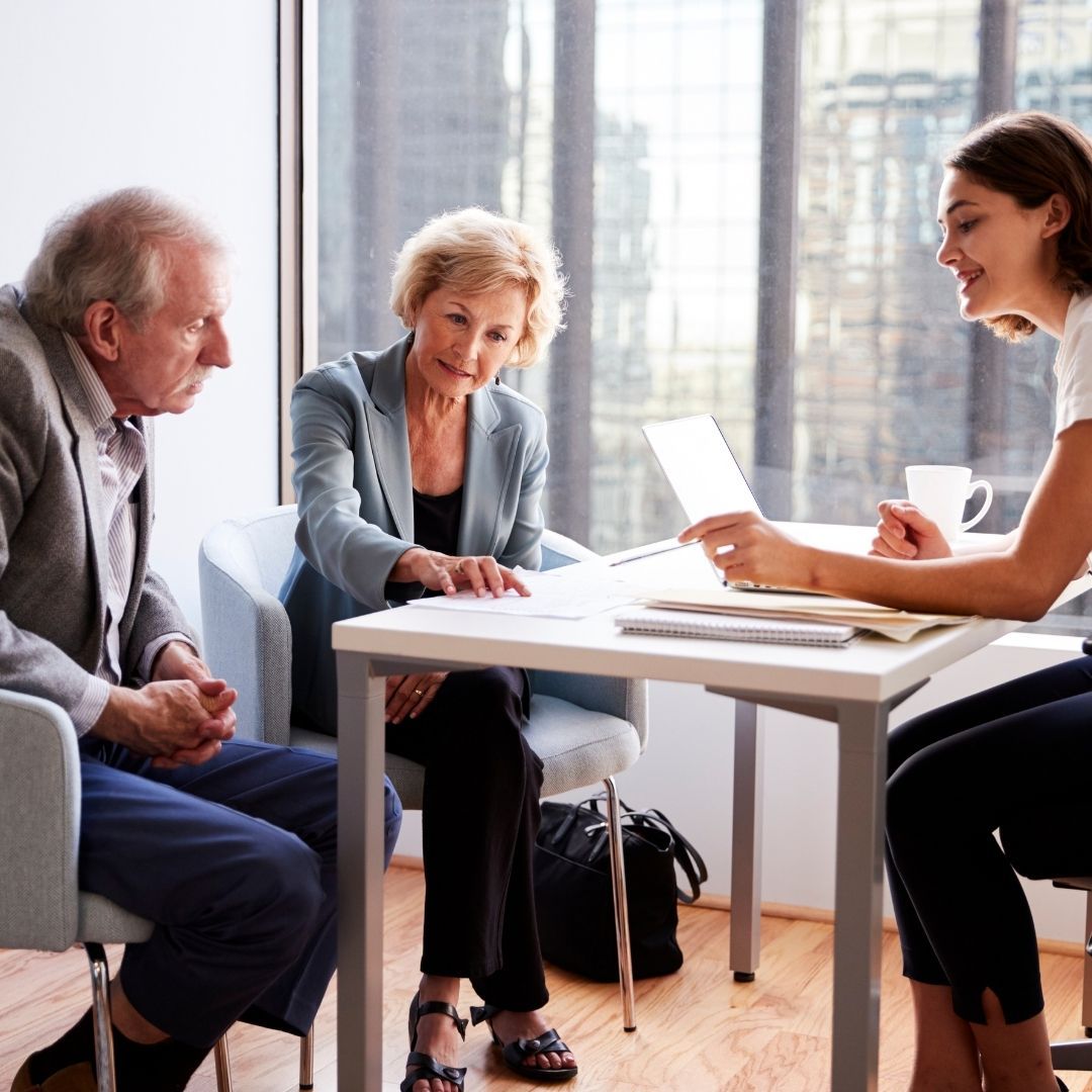 A financial advisor reviewing documents with an elderly couple in a modern office.