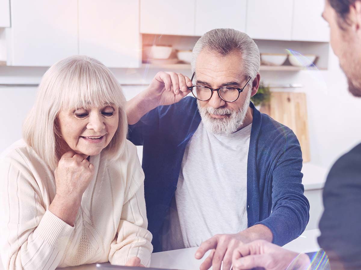 Elderly couple looking at a document with a younger person in a kitchen.