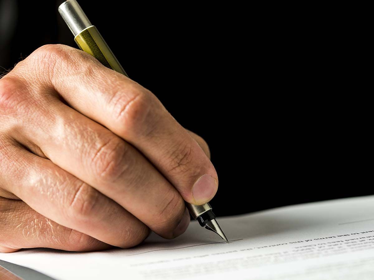 Hand writing with a pen on a document against a black background.