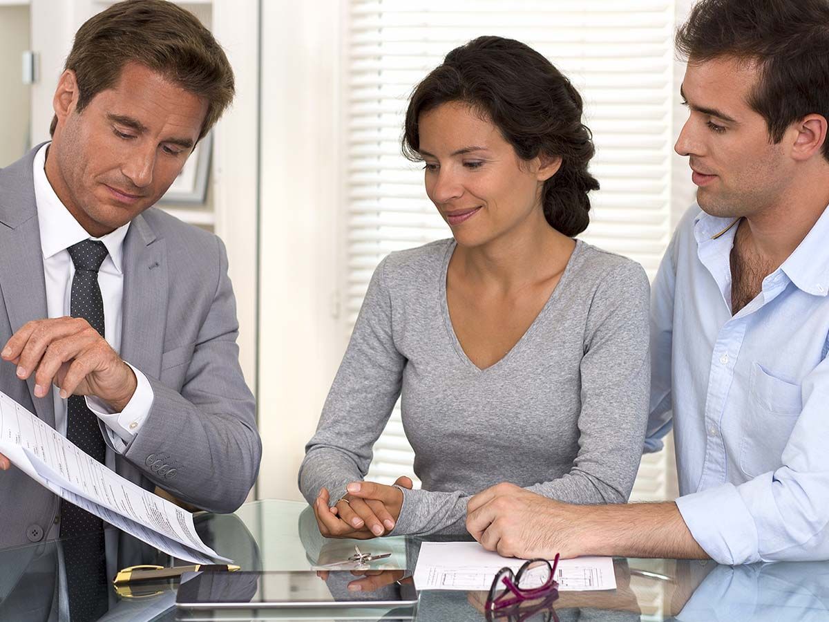 A man in a suit shows documents to a couple at a table; they are focused and attentive.
