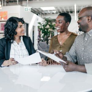 Three people at a table reviewing papers, smiling. Bright, modern office setting.