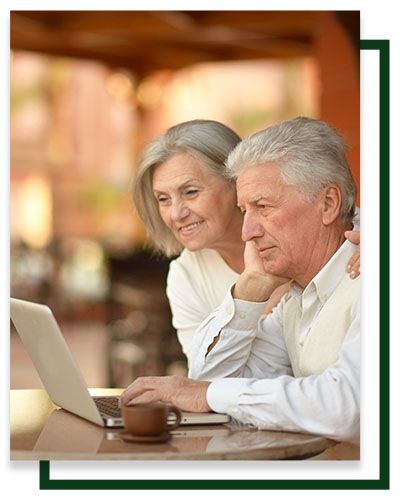 Older couple looking at laptop, one pointing, with coffee cup on table. Outdoors.