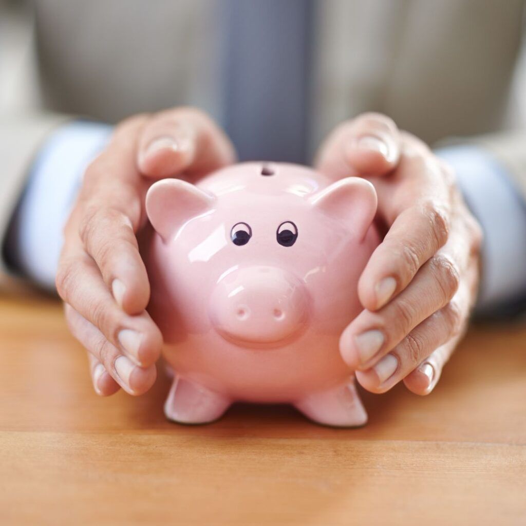 Hands gently holding a pink piggy bank on a wooden surface.