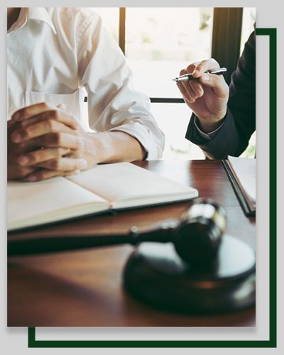 A lawyer pointing at document, discussing with client over a wooden table with gavel and notebook.