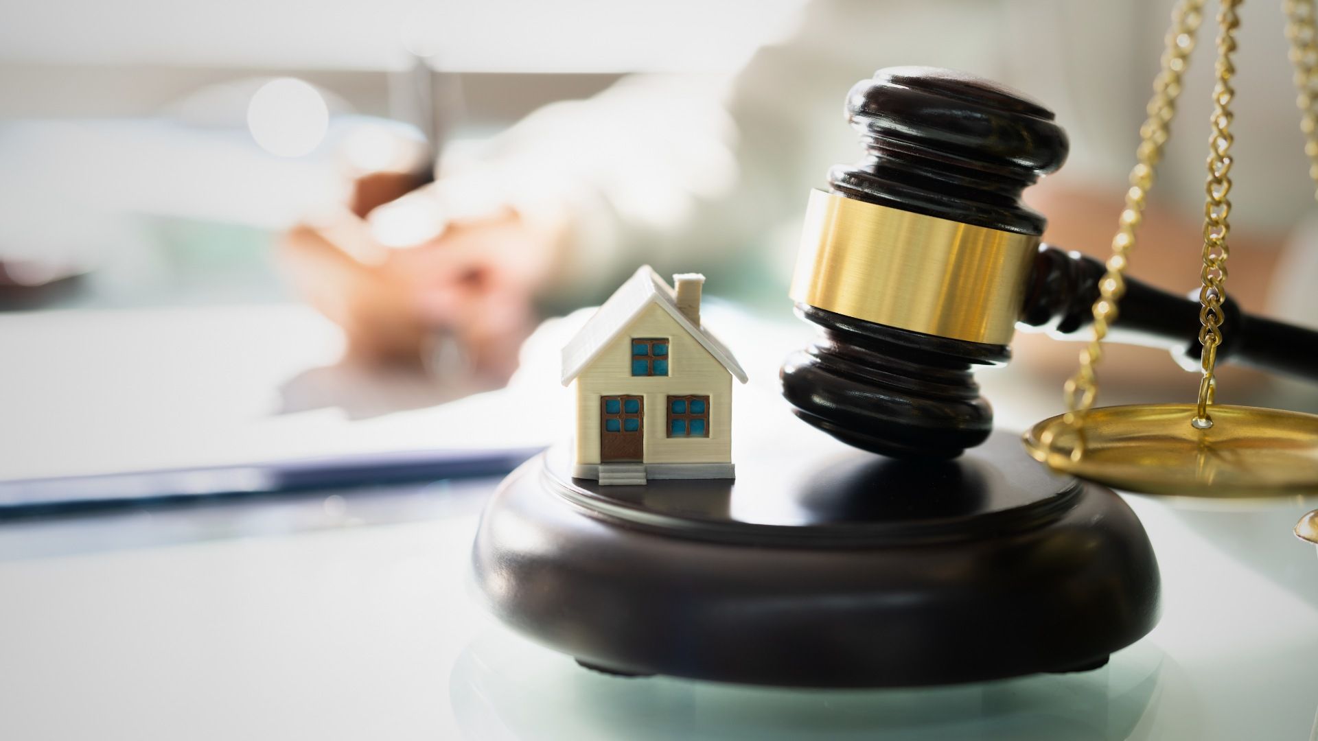 Gavel on a stand next to a toy house and scales, suggesting a real estate legal matter.