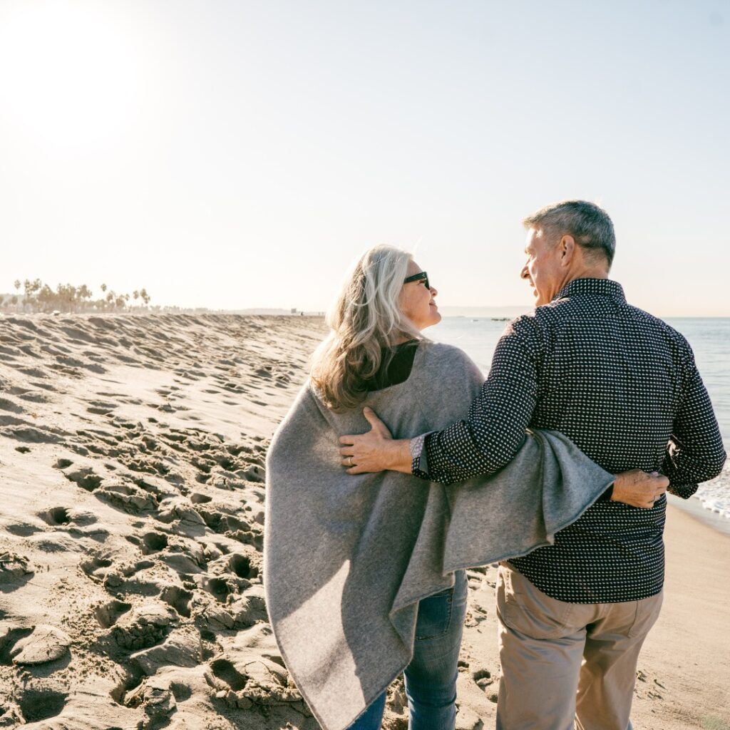 Couple walking on beach, man with arm around woman, sunny day.