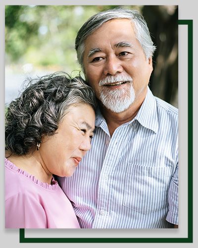Smiling older couple embracing outdoors. Woman resting head on man's shoulder.
