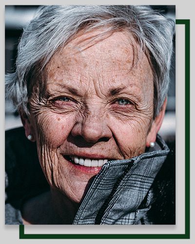 Smiling person with short, gray hair; light eyes; and wrinkles; wearing a gray jacket.